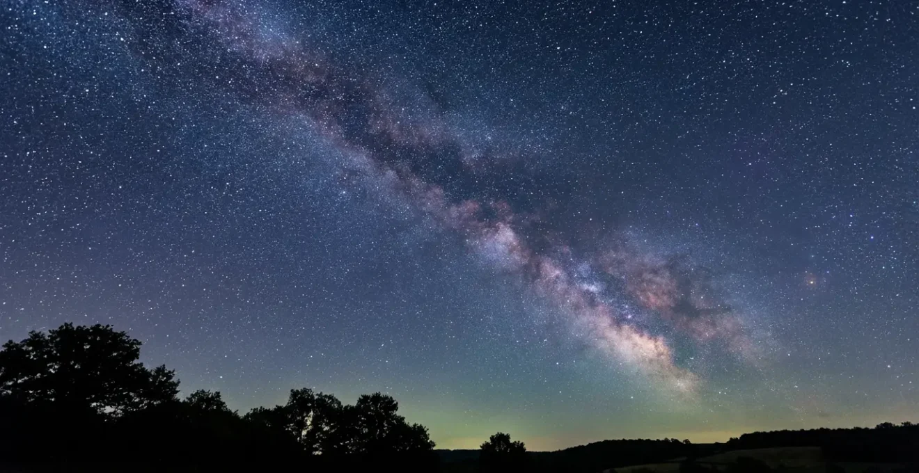 Ciel étoilé nocturne avec la Voie Lactée visible au-dessus d'un paysage rural sombre