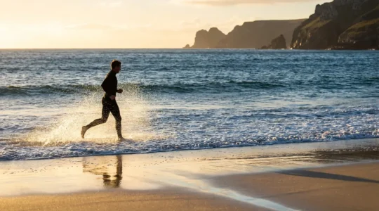 Marcheur solitaire sur une plage sauvage au lever du soleil avec les vagues et les embruns marins