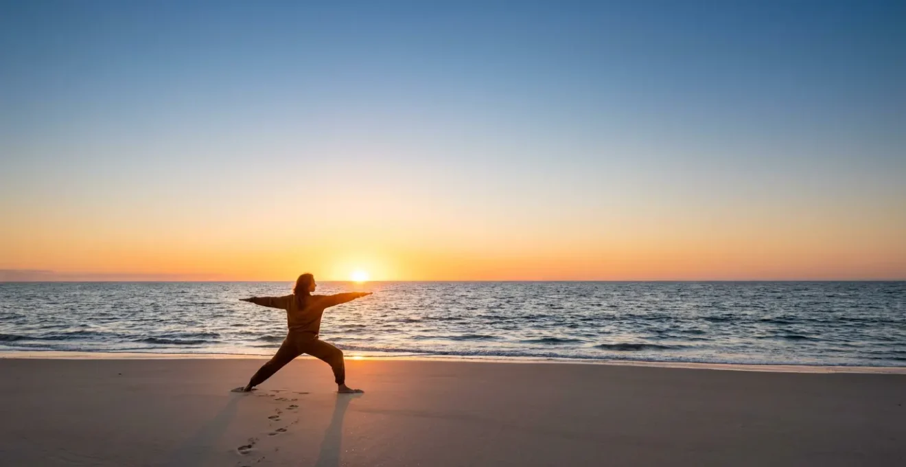 Pratique de yoga matinale face à la mer, une personne en posture du guerrier sur le sable au lever du soleil